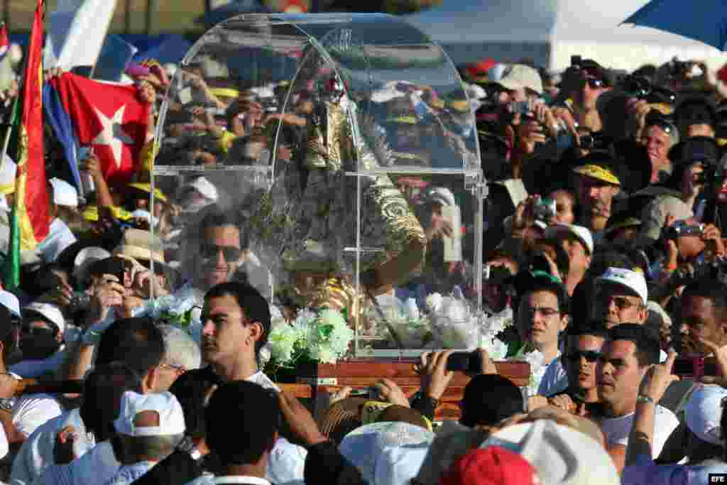 Un grupo de hombres carga una imagen de la Virgen de la Caridad entre cientos de personas que asisten a la una misa multitudinaria.